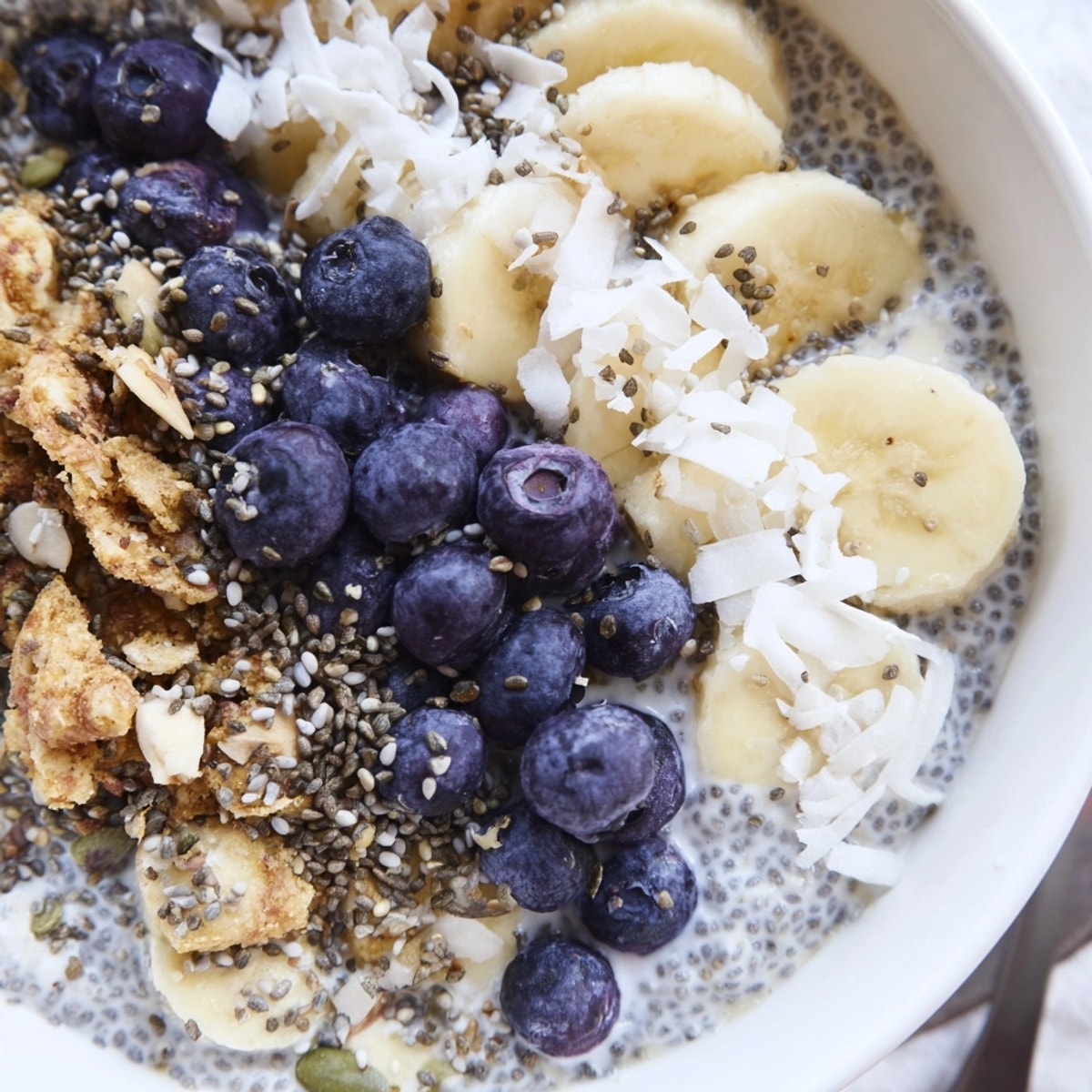 Close-up of a Blueberry Chia Breakfast Bowl swirled with almond milk and bursting with juicy blueberries.