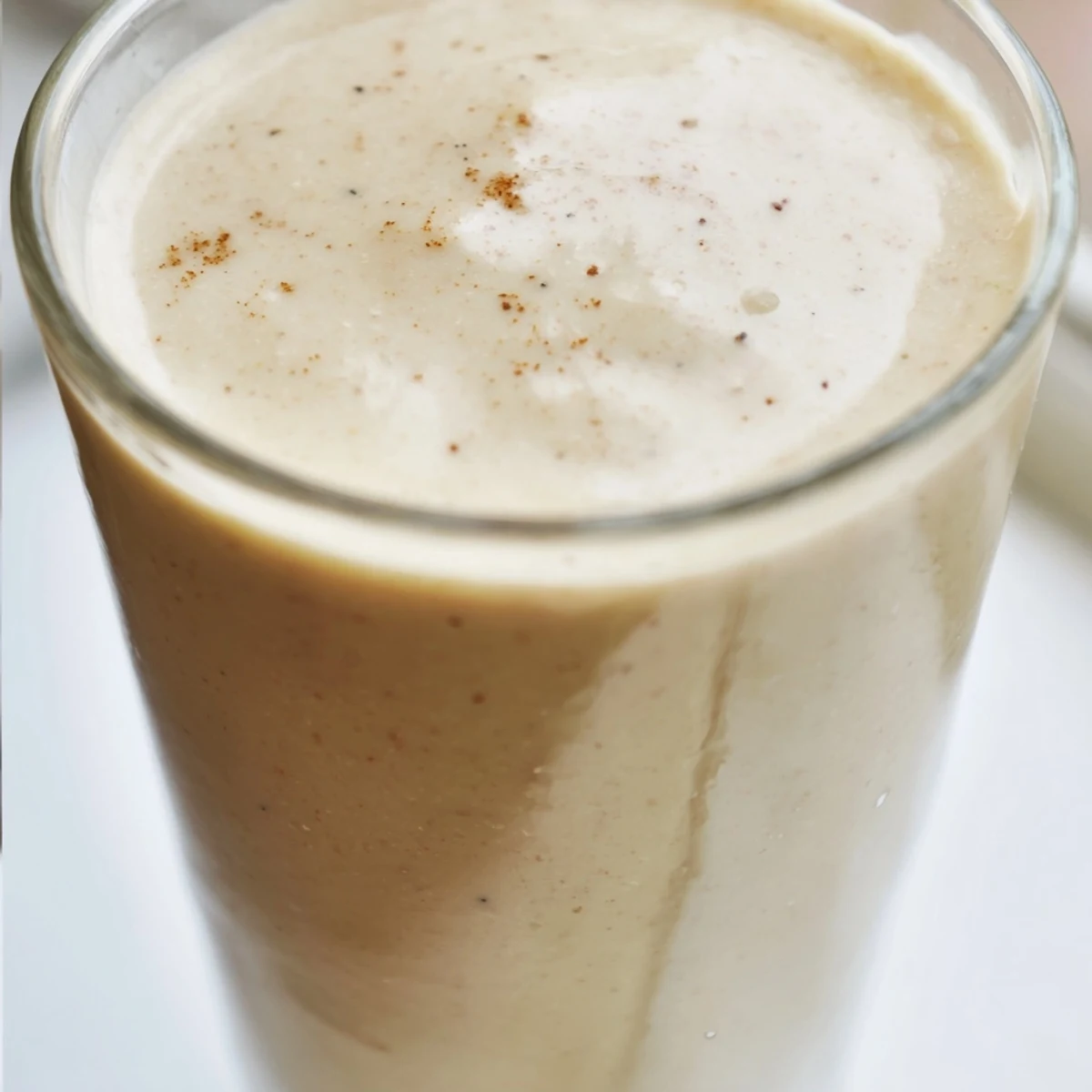 Thick and frothy Cozy Apple Smoothie topped with nutmeg, served beside sliced apples on a rustic table.