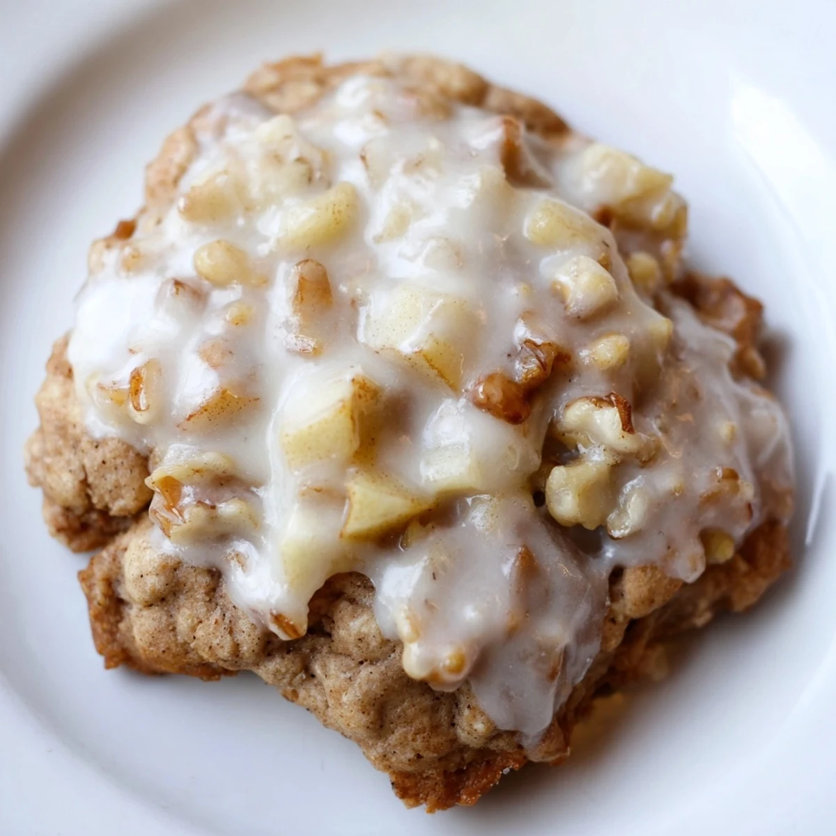 Freshly baked Frosted Apple Cookies on a white plate with diced apples nearby.