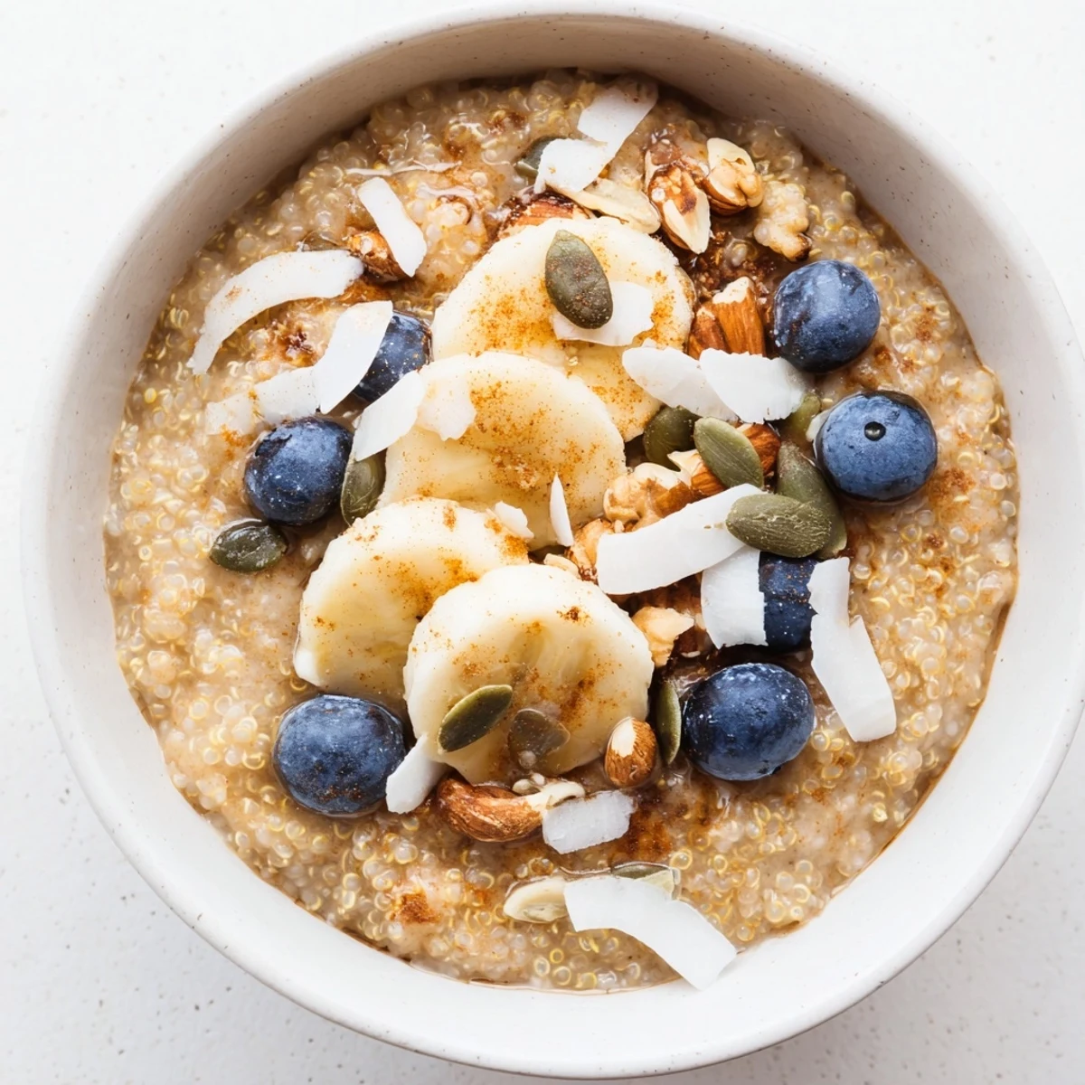 A close-up of creamy Vegan Quinoa Porridge topped with sliced banana, fresh berries, and pumpkin seeds. 