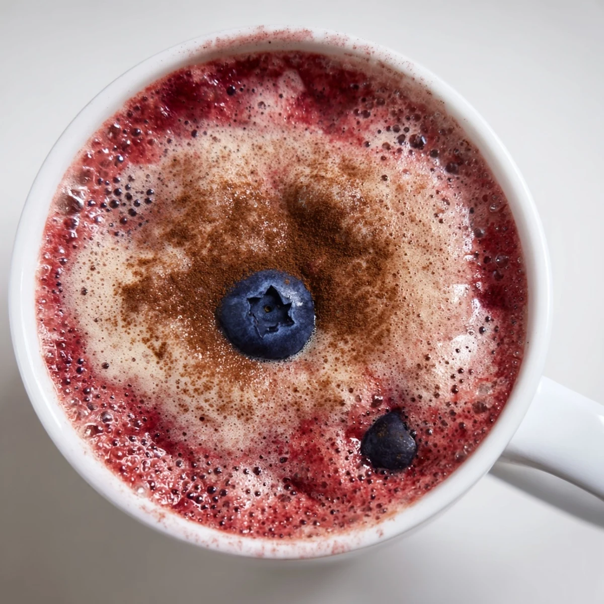 A comforting cup of Warm Berry Smoothie topped with fresh berries, steaming gently on a wooden table.