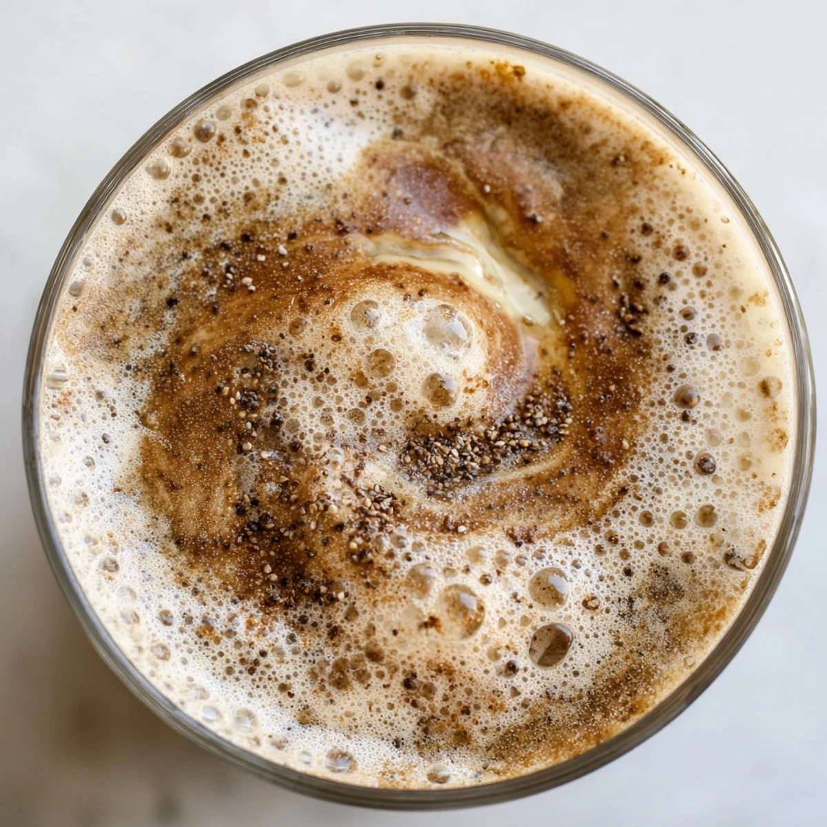 Close-up shot of a glass Vegan Maple Smoothie next to maple syrup and a sliced banana on a rustic wooden table.