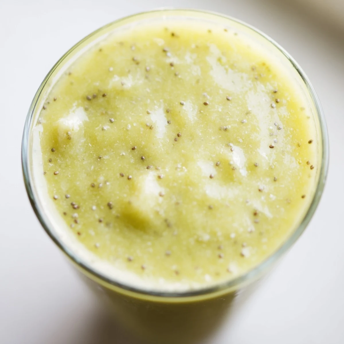 Two glasses of Bright Apple Smoothie garnished with apple slices and a cinnamon stick on a bright kitchen counter.