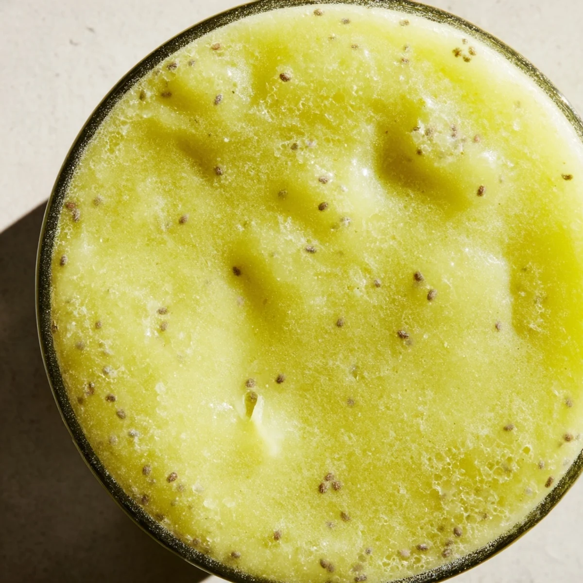 A tall glass of Bright Apple Smoothie, filled with vibrant yellow-orange liquid and topped with chia seeds.