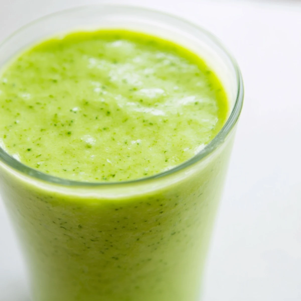 A refreshing glass of Bright Spinach Smoothie beside a bowl of tropical fruit, perfect for breakfast.