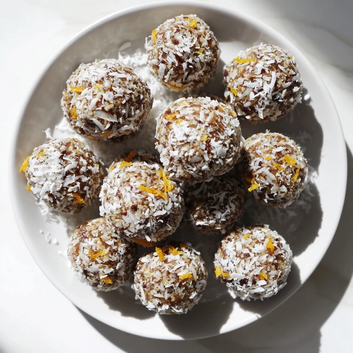 A close-up of Wholesome Citrus Bites, coated in shredded coconut and garnished with fresh lemon and orange zest for a bright, zesty flavor.