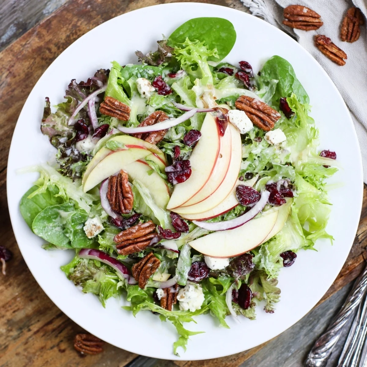 Overhead view of Crisp Maple Salad showcasing glossy apple slices, golden toasted pecans, and vibrant greens tossed in homemade maple vinaigrette with crumbled cheese.
