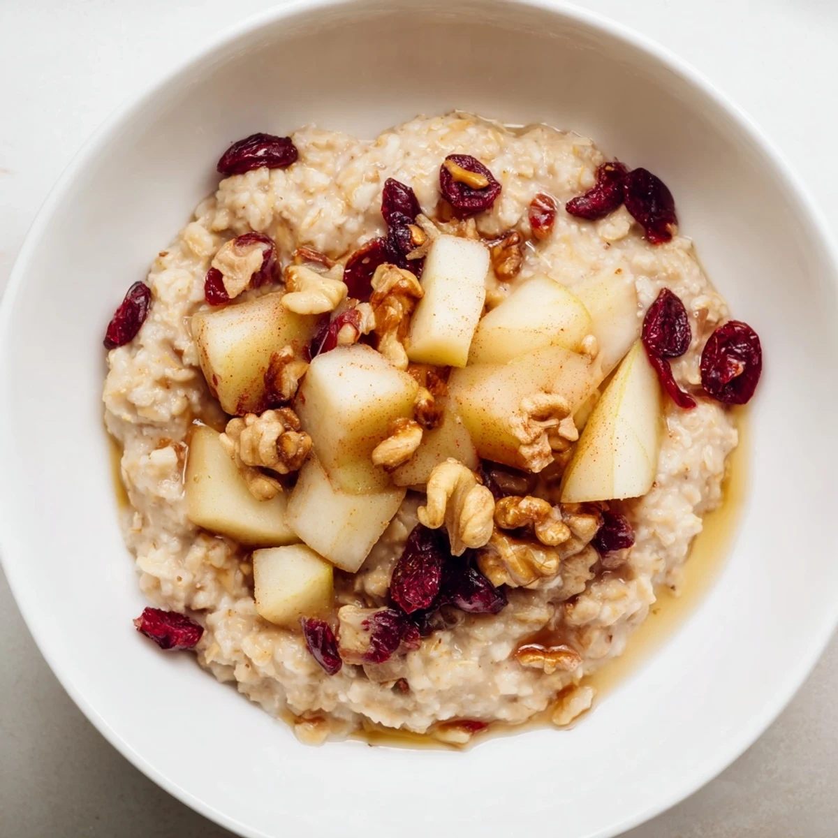 Two servings of Festive Pear Porridge topped with toasted walnuts, dried cranberries, and a sweet maple drizzle.
