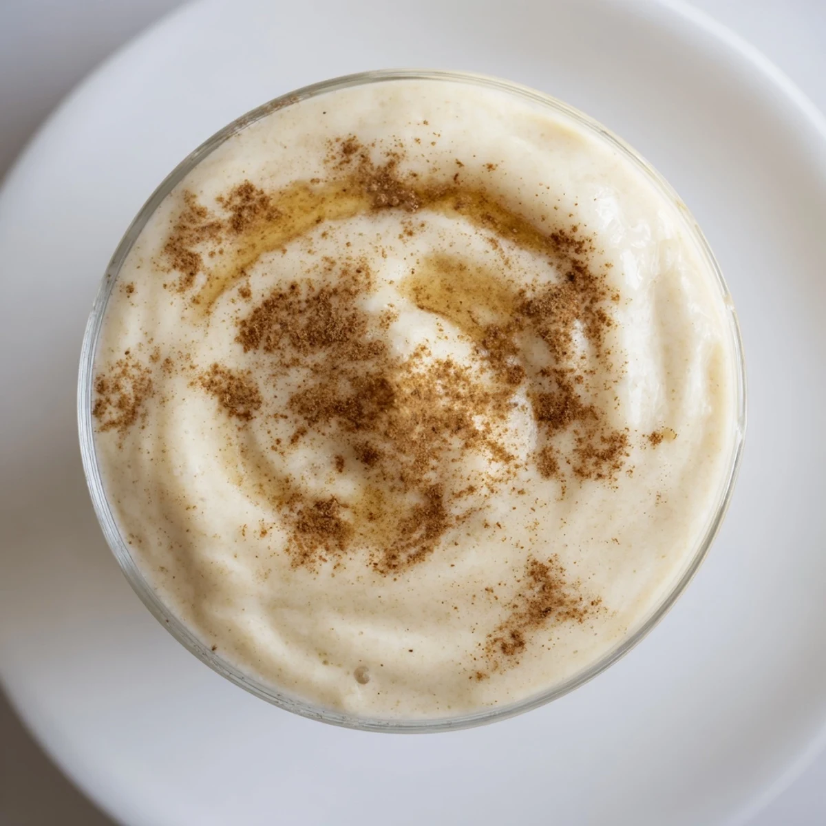 Two glasses of Frosted Maple Smoothie next to a sliced banana and maple syrup bottle.