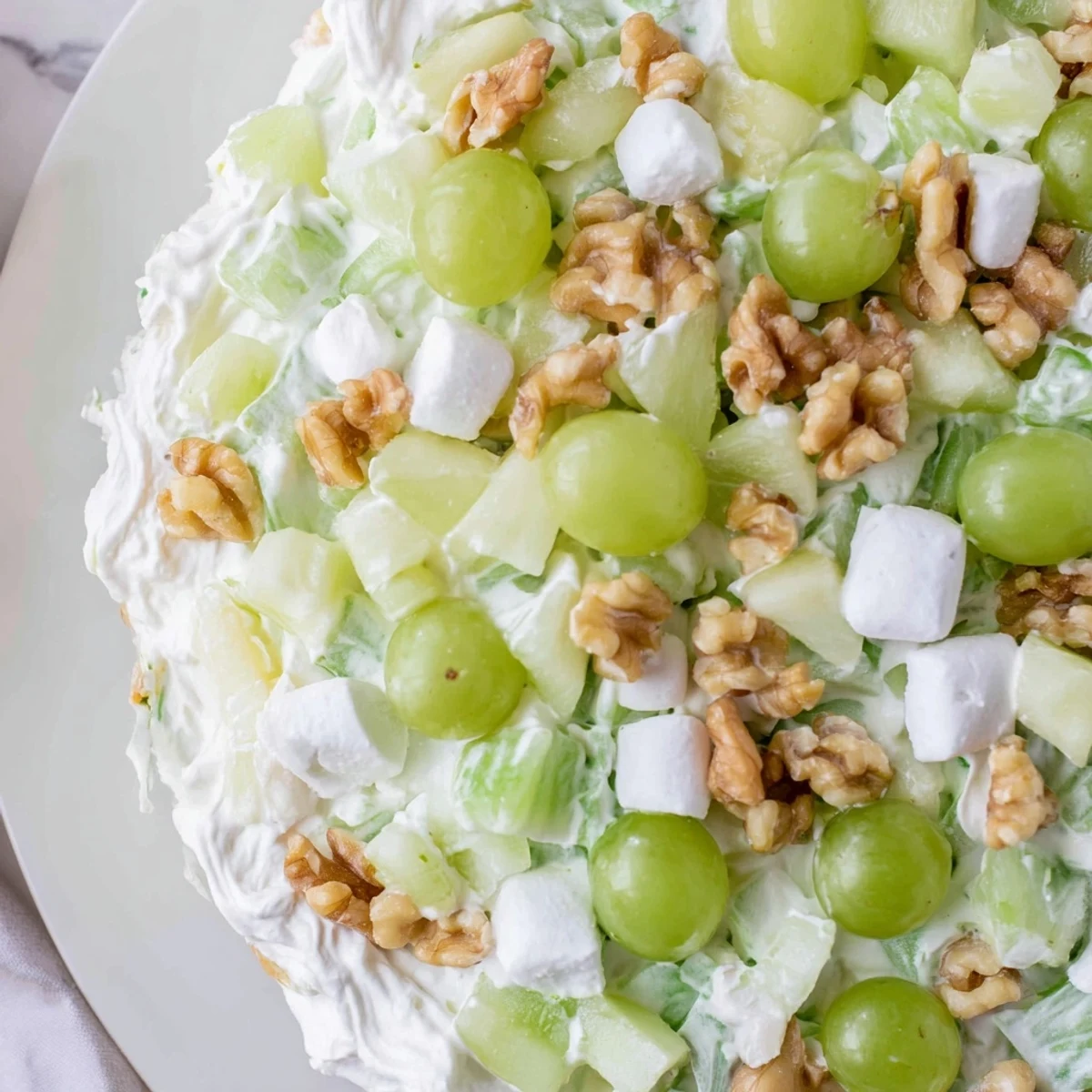 A frosted green salad with creamy pineapple dressing, fresh grapes, and crisp apples served in a glass bowl.