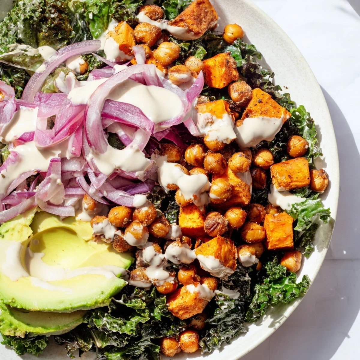 Golden roasted sweet potatoes and crispy chickpeas sit atop sautéed kale in this vibrant Cozy Kale Bowl, drizzled with creamy tahini dressing.  