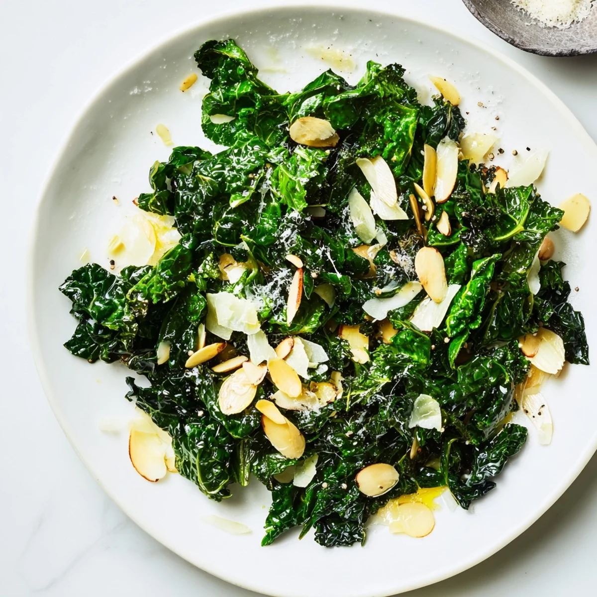A close-up of vibrant green Warm Kale Treat with golden garlic slices and toasted nuts, ready to serve as a healthy side.  
