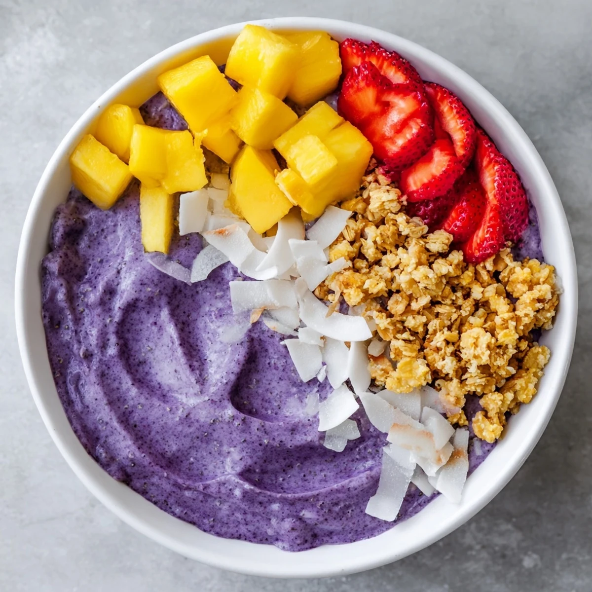 Creamy ube coconut chia breakfast bowl garnished with strawberries and toasted coconut flakes.