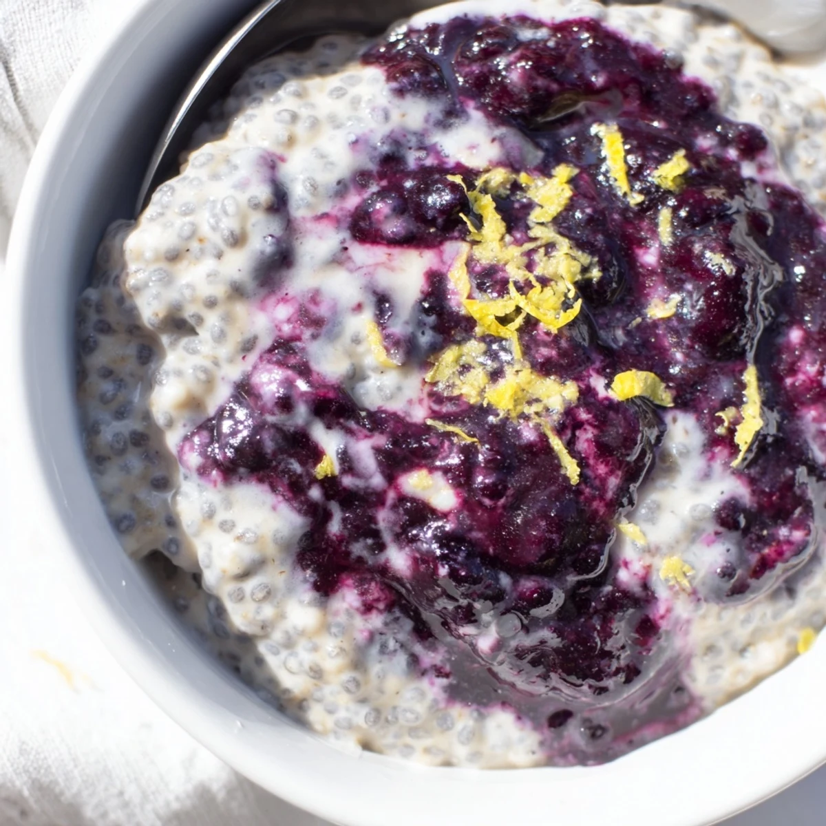 A creamy Blueberry Lemon Cheesecake Chia Breakfast Bowl swirled with cream cheese and compote.