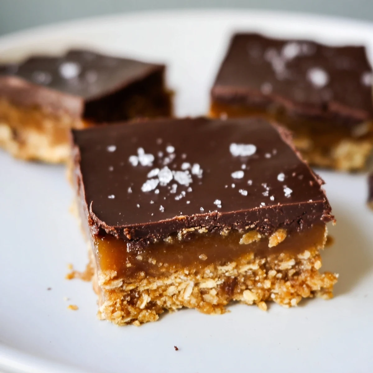 A close-up view of Salted Date Caramel Sweet Treat Squares, revealing a luscious date caramel layer on a crisp almond-oat base, finished with flaky sea salt.