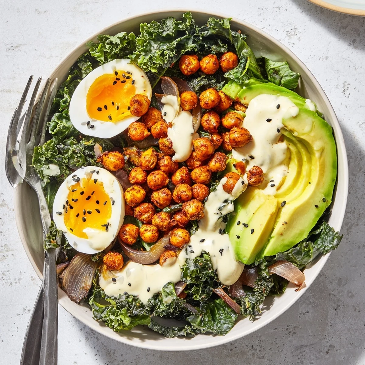 Bright avocado slices and toasted sesame seeds garnish the Savory Tahini Kale Breakfast Bowl with Crispy Chickpeas