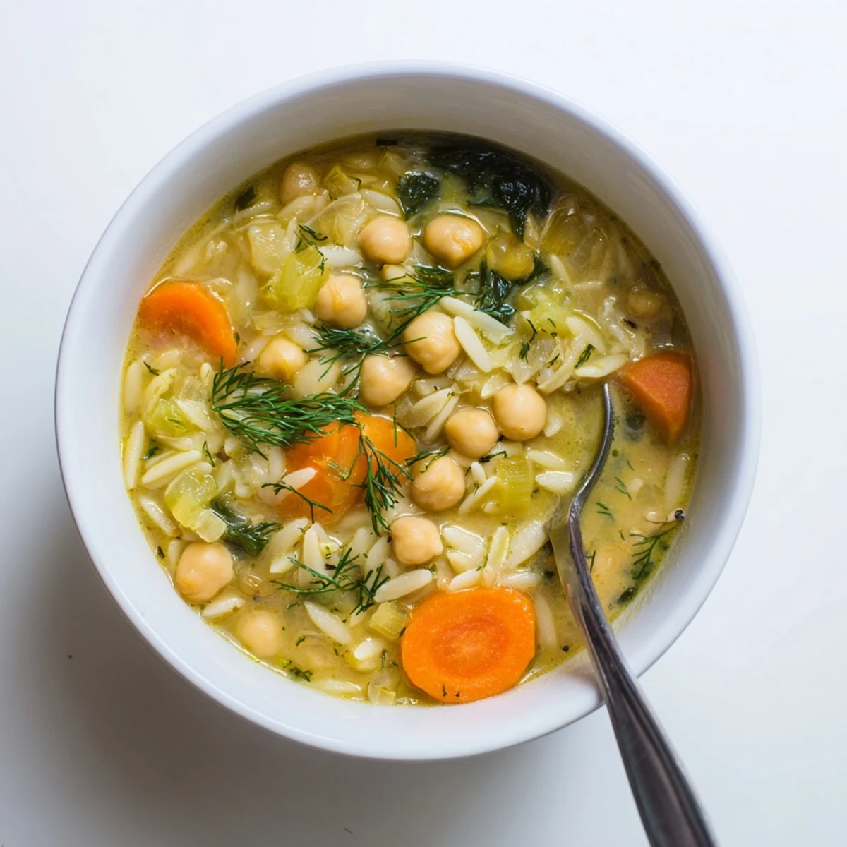 Creamy Lemon Chickpea Orzo Hearty Soup steaming in a rustic bowl with spinach and lemon garnish.