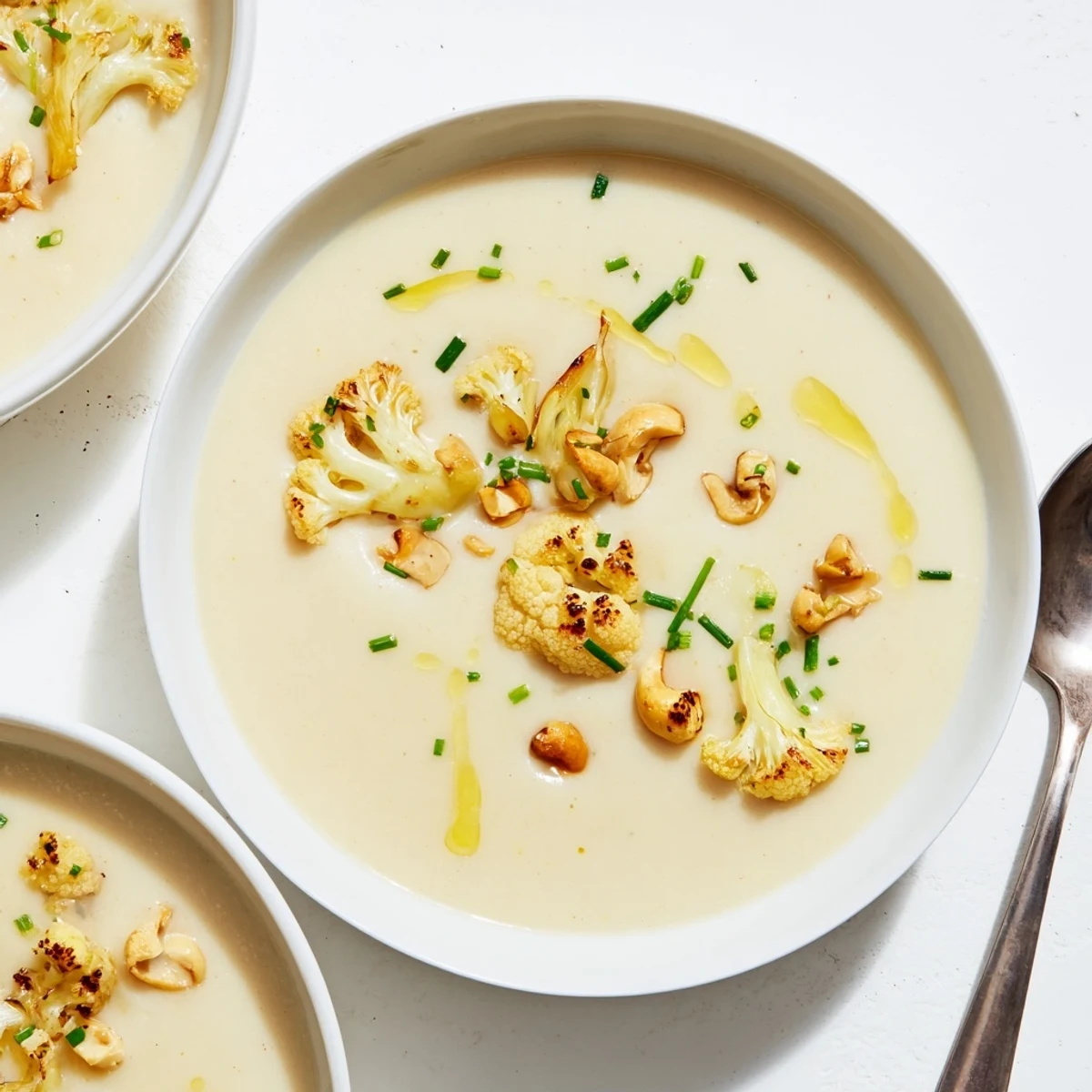 A steaming bowl of Roasted Garlic Cauliflower Cashew Hearty Soup served alongside crusty bread on a cozy table.