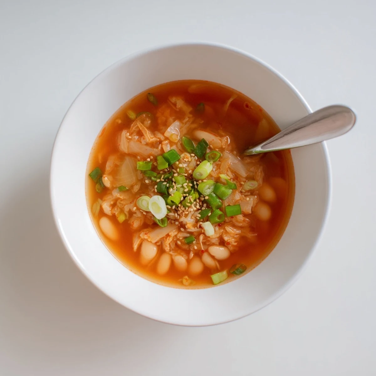 Overhead view of Spicy Kimchi White Bean Hearty Soup simmering in a pot, featuring creamy white beans and chopped vegetables.