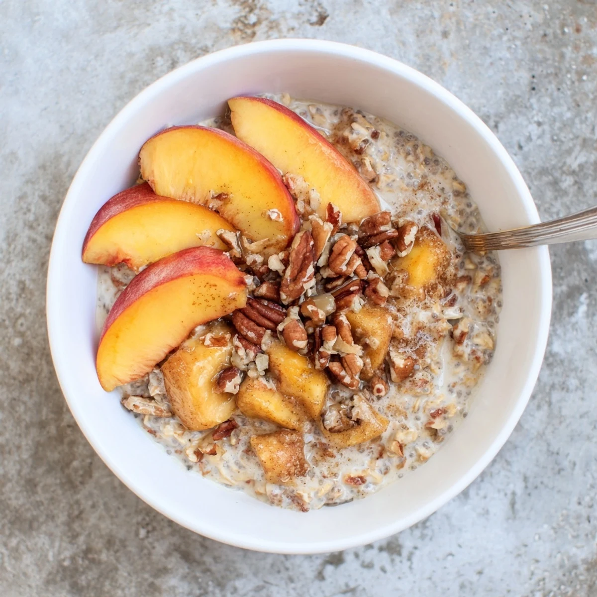 Chilled Peach Cobbler Overnight Oats Breakfast Bowl served in a ceramic bowl with granola and fresh peach slices garnish.
