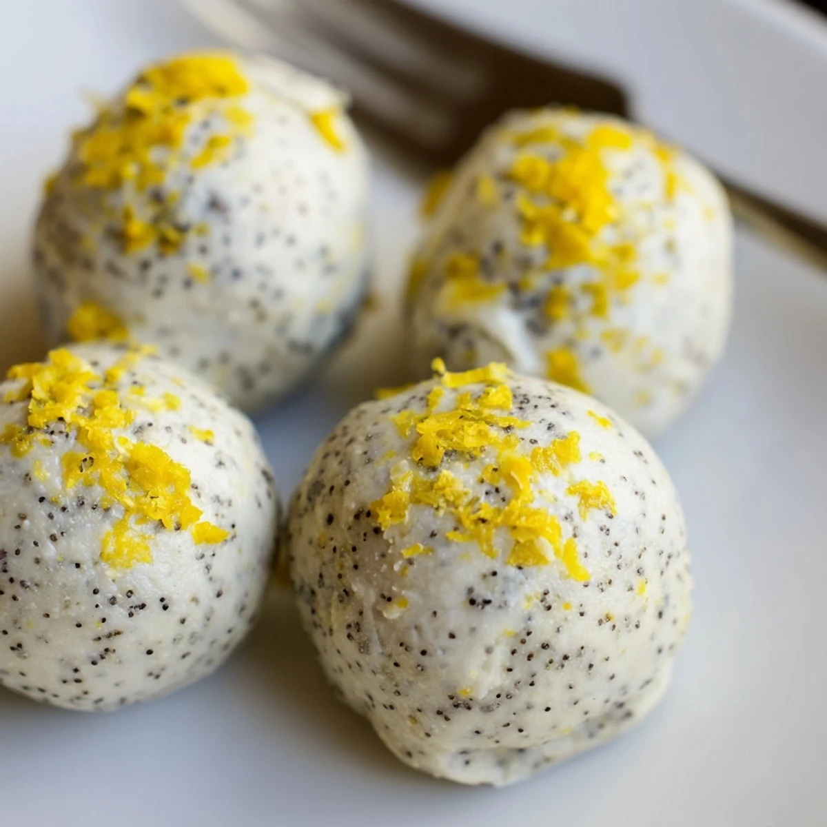 A close-up of Lemon Poppy Seed Cashew Bliss Sweet Treat bites on a chilled plate, garnished with fresh lemon zest.