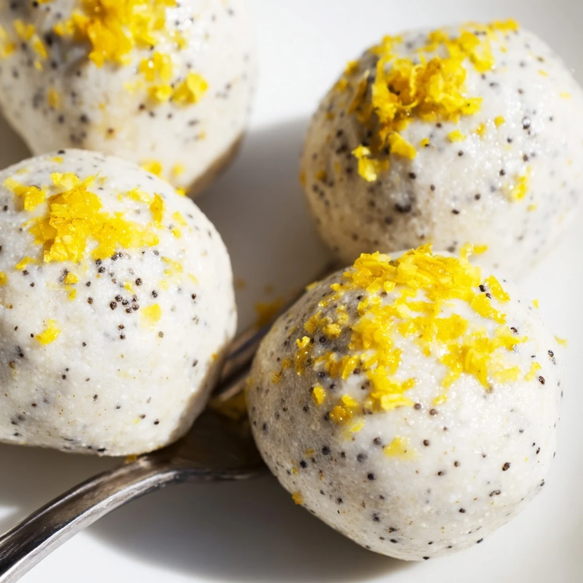 A hand reaching for a creamy Lemon Poppy Seed Cashew Bliss Sweet Treat bite next to a cup of herbal tea.