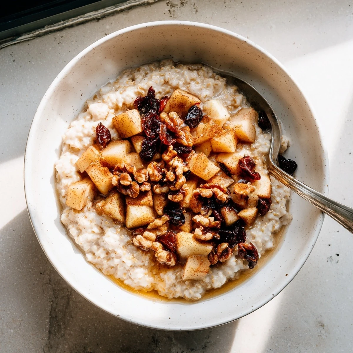 Spoonful of apple pie steel cut oat breakfast bowl featuring tender cinnamon apples and dried cranberries