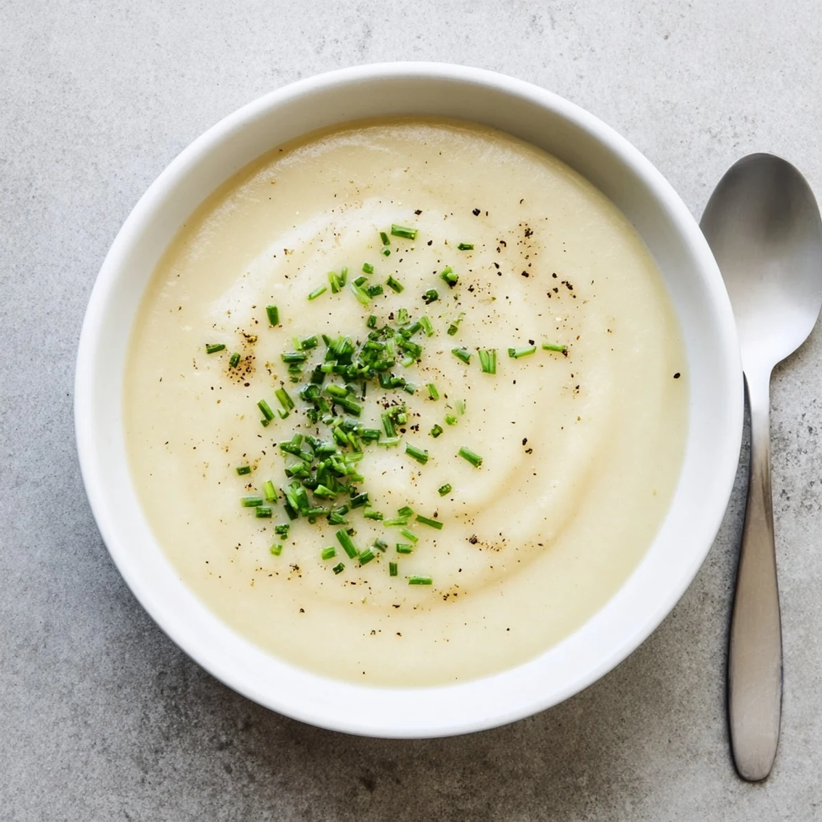 Creamy celery root and leek soup garnished with fresh chives in a white bowl