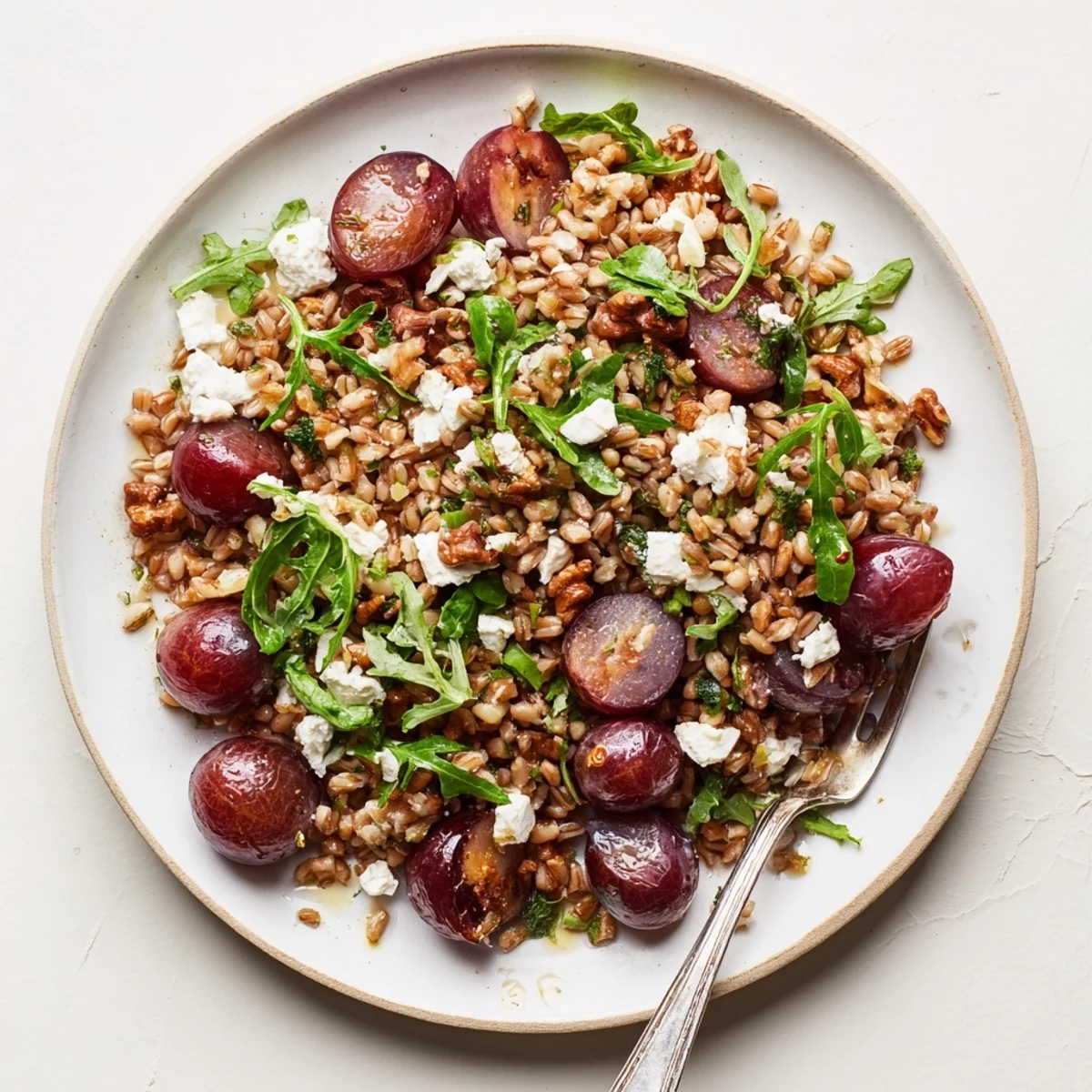 Colorful roasted grape and walnut farro grain salad plated on white serving dish