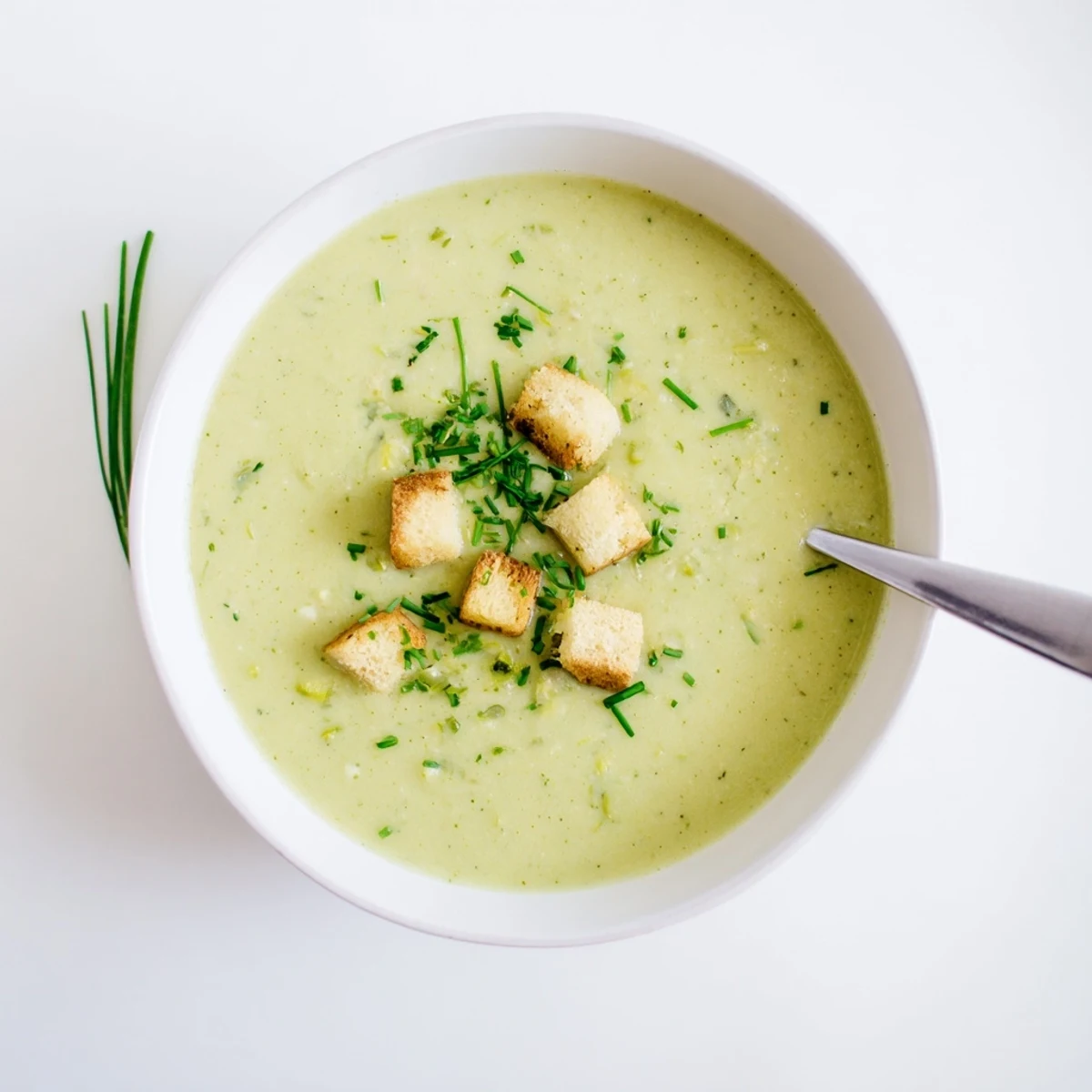 Smooth vegetarian zucchini soup with roasted garlic floating beside crusty bread slice