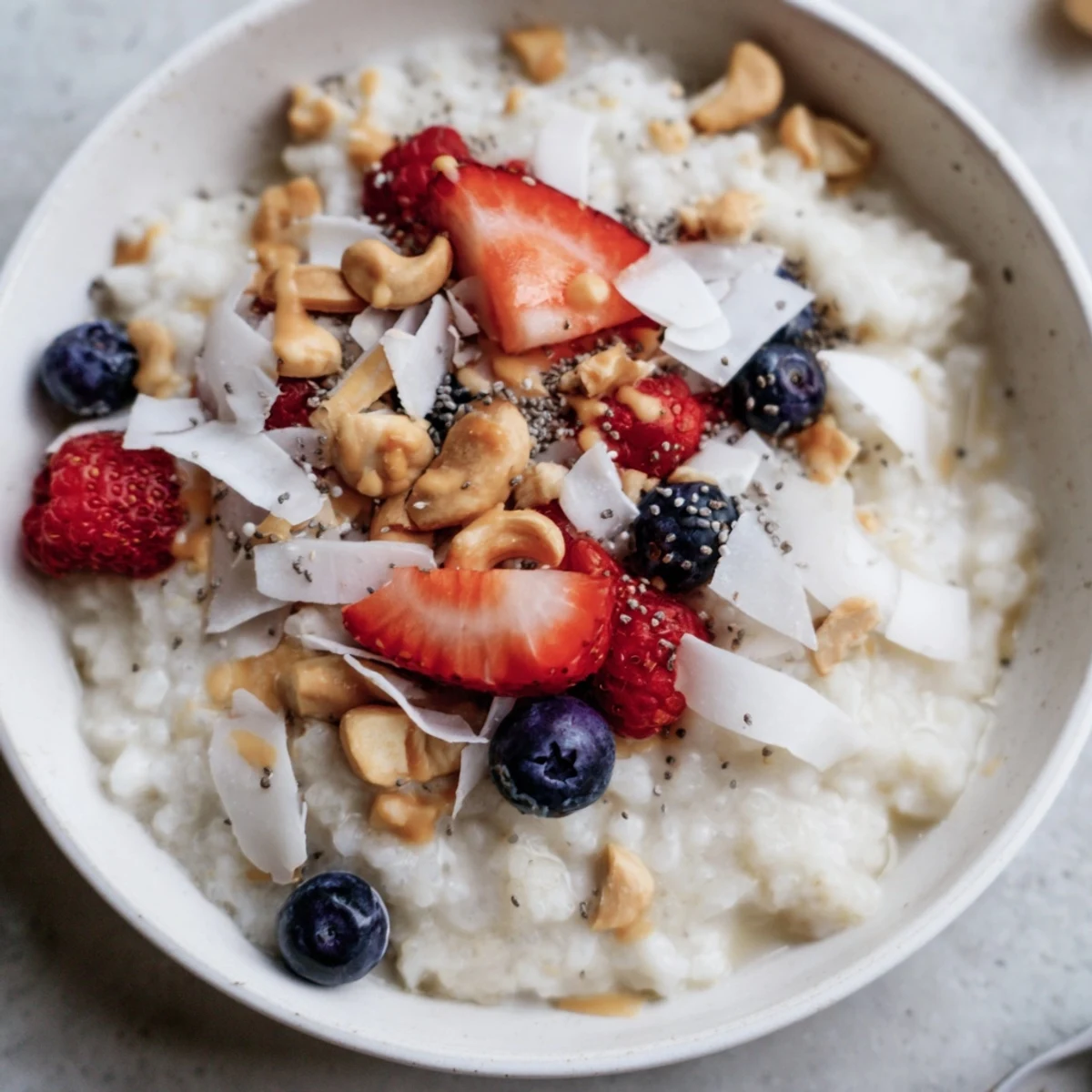 Creamy vanilla coconut rice pudding breakfast bowl topped with fresh mixed berries and toasted coconut flakes