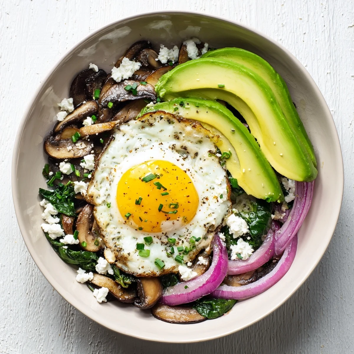 Savory breakfast bowl featuring sautéed vegetables, creamy avocado slices, and a runny yolk egg