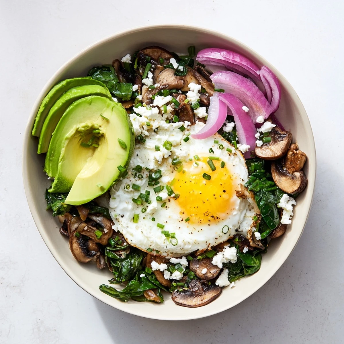 Hearty spinach mushroom breakfast bowl in a white bowl with fresh herbs and crumbled feta