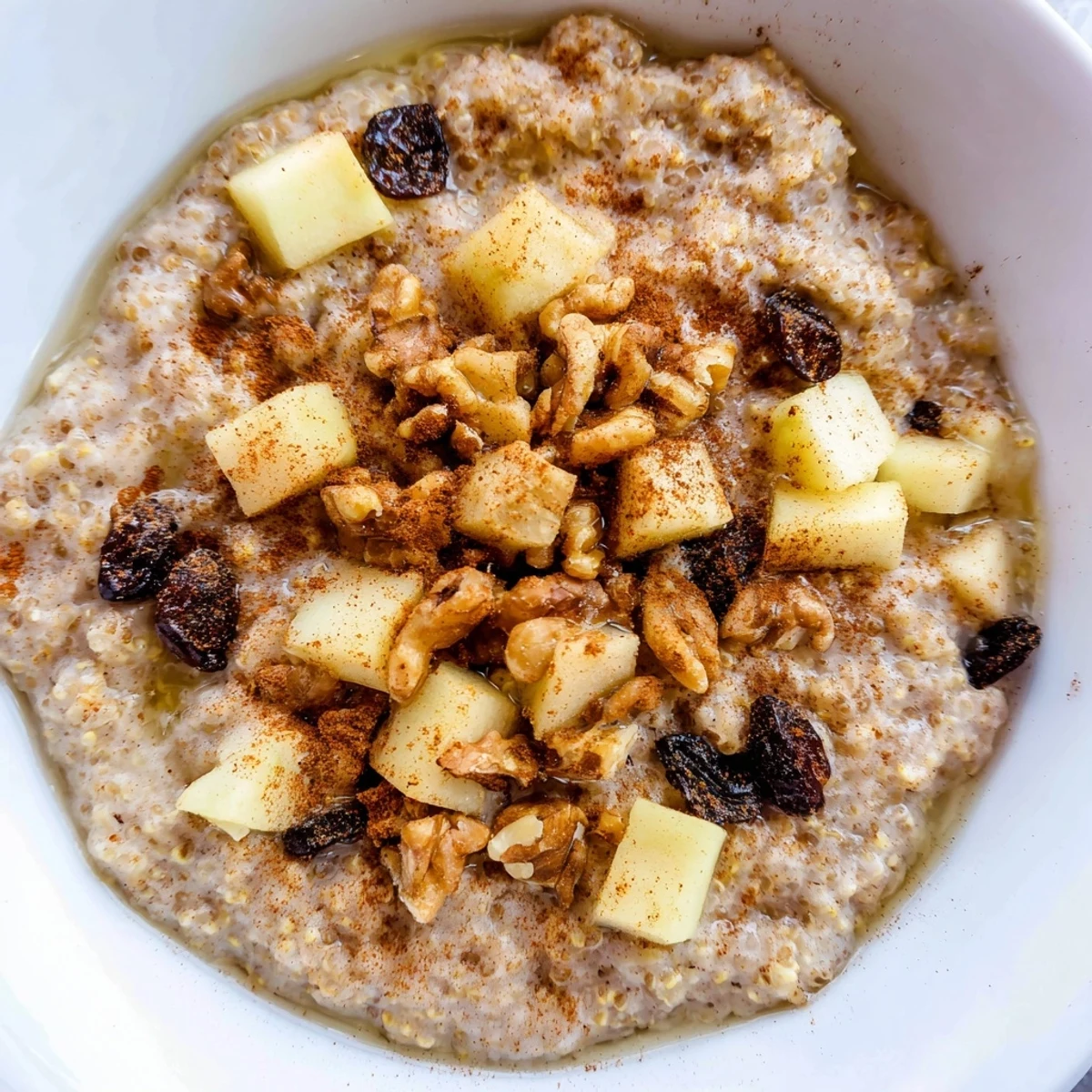 Warm apple cinnamon quinoa porridge bowl topped with crunchy walnuts and sweet maple drizzle