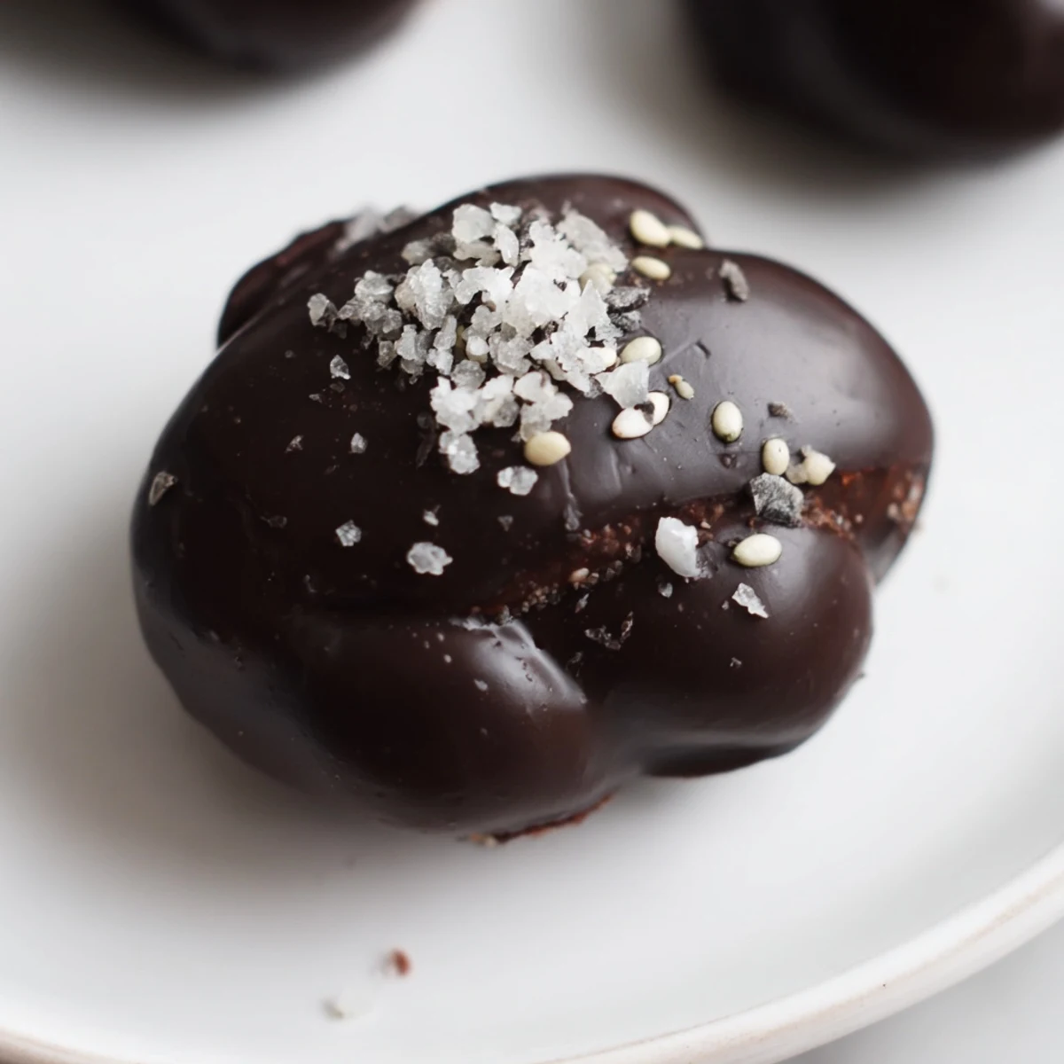 Bite-sized dark chocolate sesame date clusters sprinkled with sea salt on a white plate