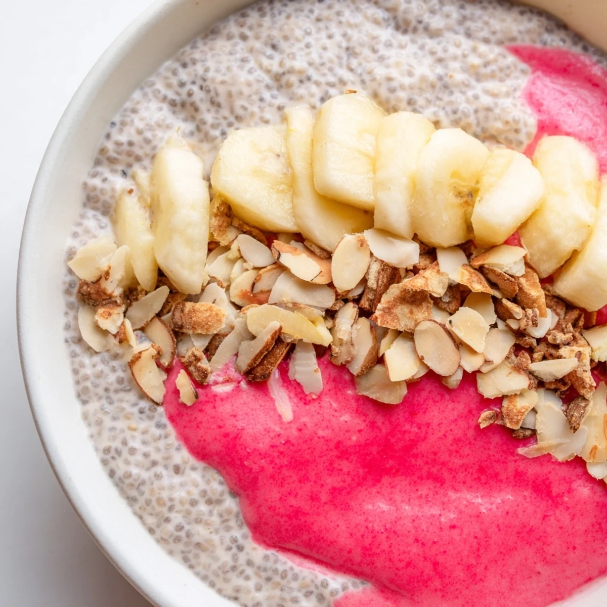 Vibrant pink guava coconut vanilla chia breakfast bowl layered with banana slices and crunchy almonds