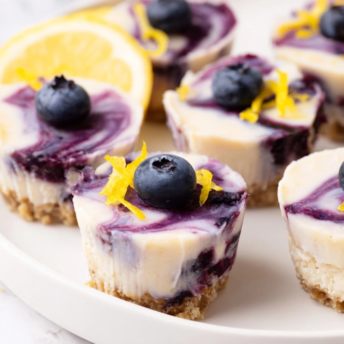 Mini no-bake blueberry lemon cashew cheesecake bites with marbled fruit topping on golden date-nut base