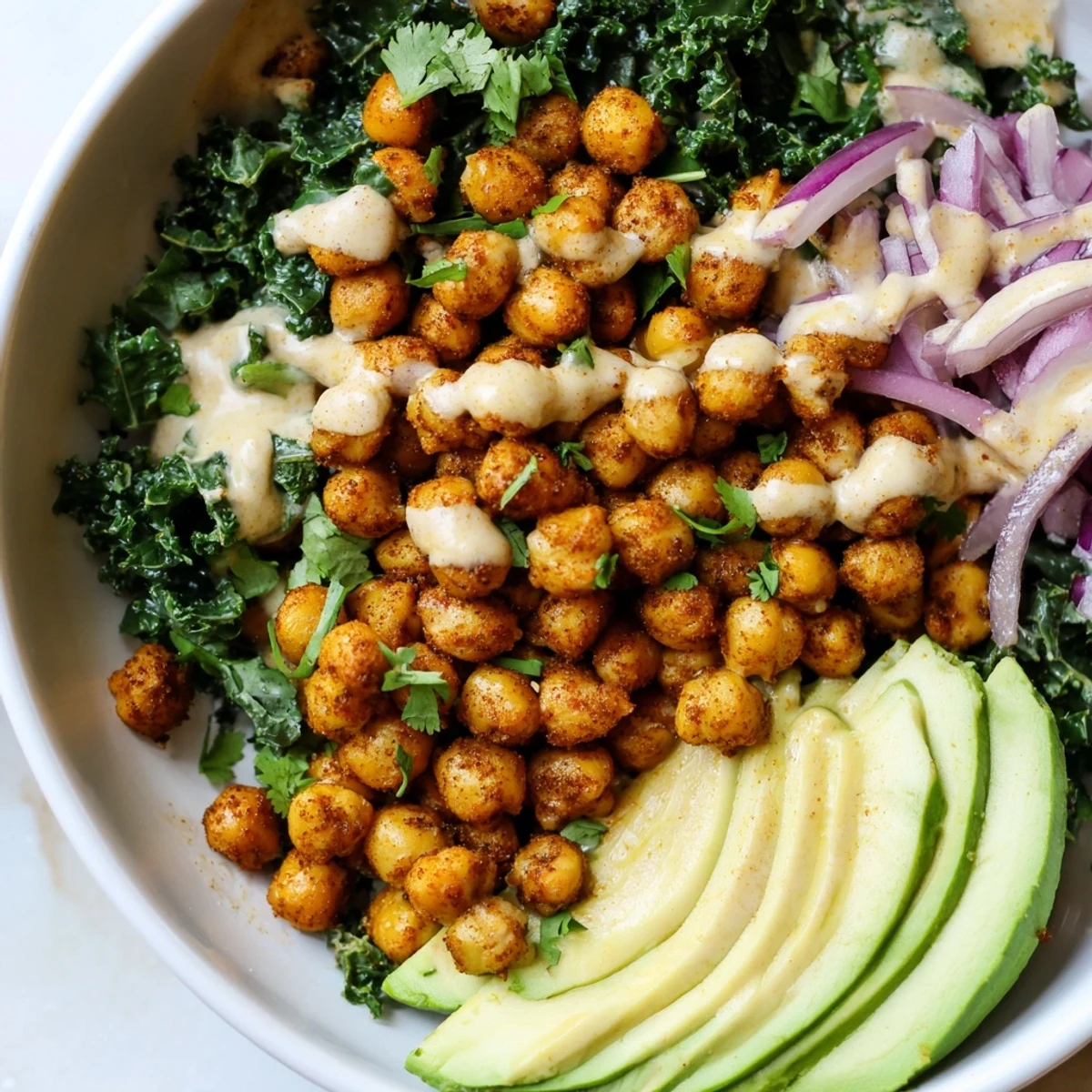 Savory Spiced Chickpea and Kale Breakfast Bowl topped with creamy avocado slices and tahini drizzle