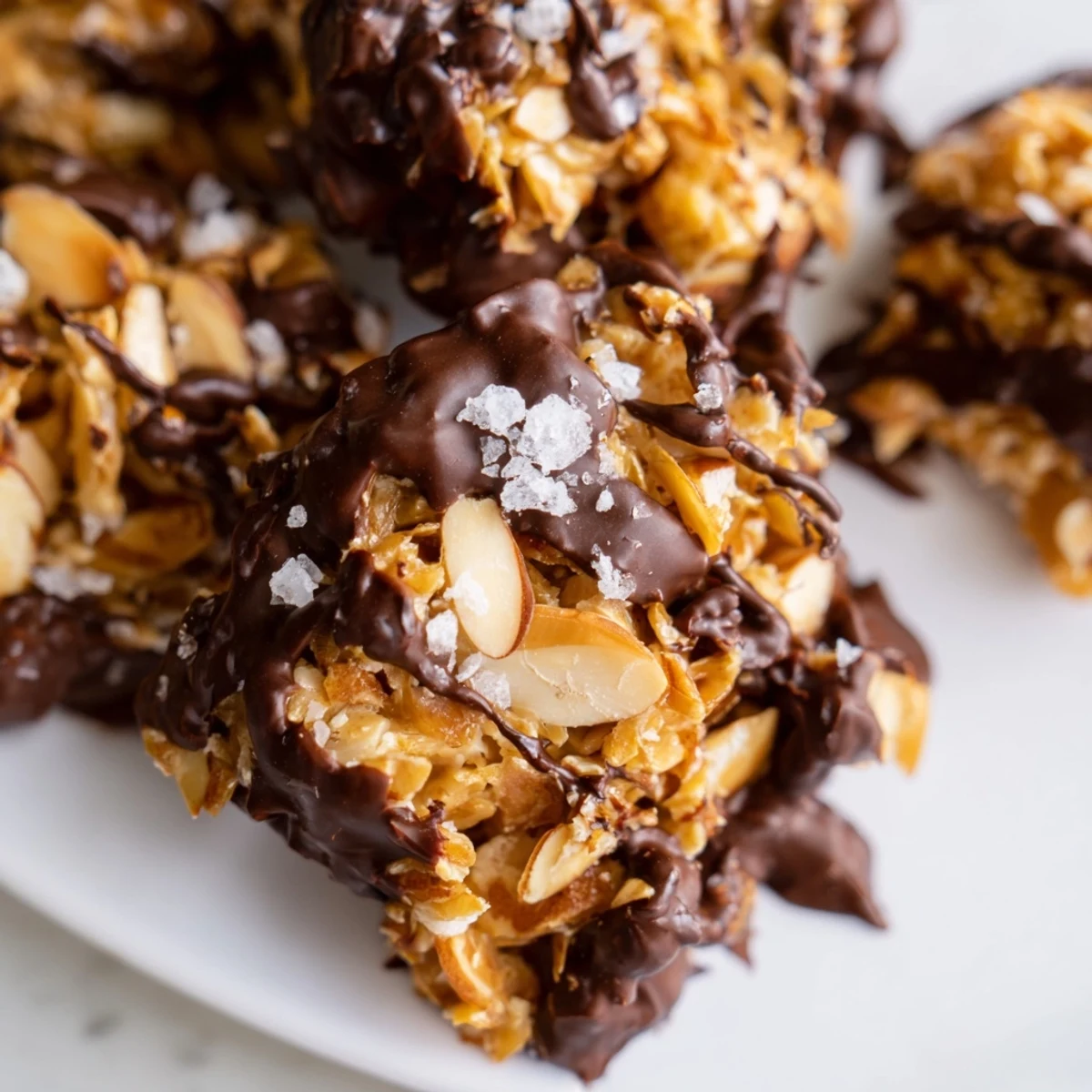 Homemade dark chocolate almond butter coconut clusters drizzled with melted chocolate and topped with flaky sea salt