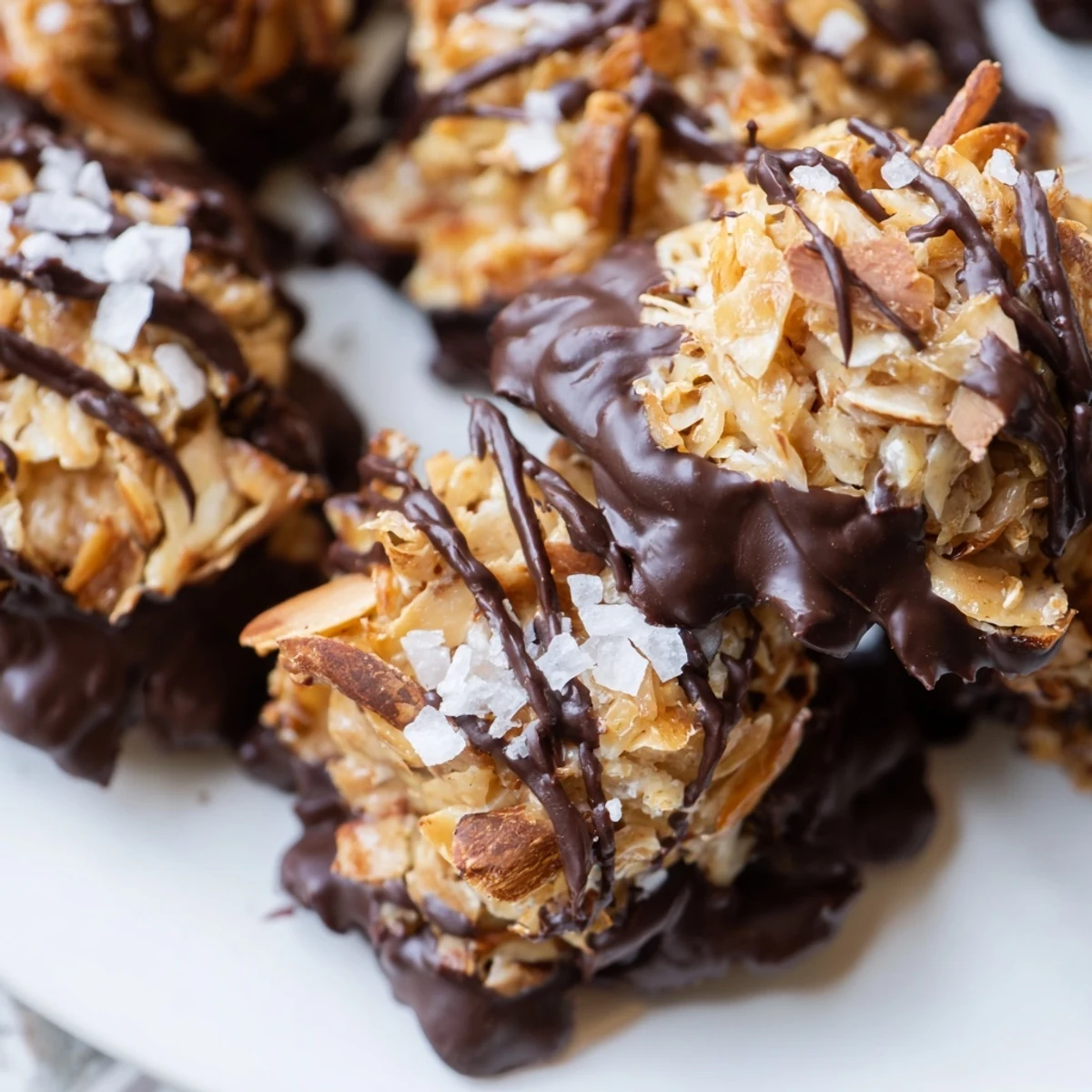 Glossy dark chocolate almond butter coconut clusters sprinkled with extra almonds ready for serving on a white plate