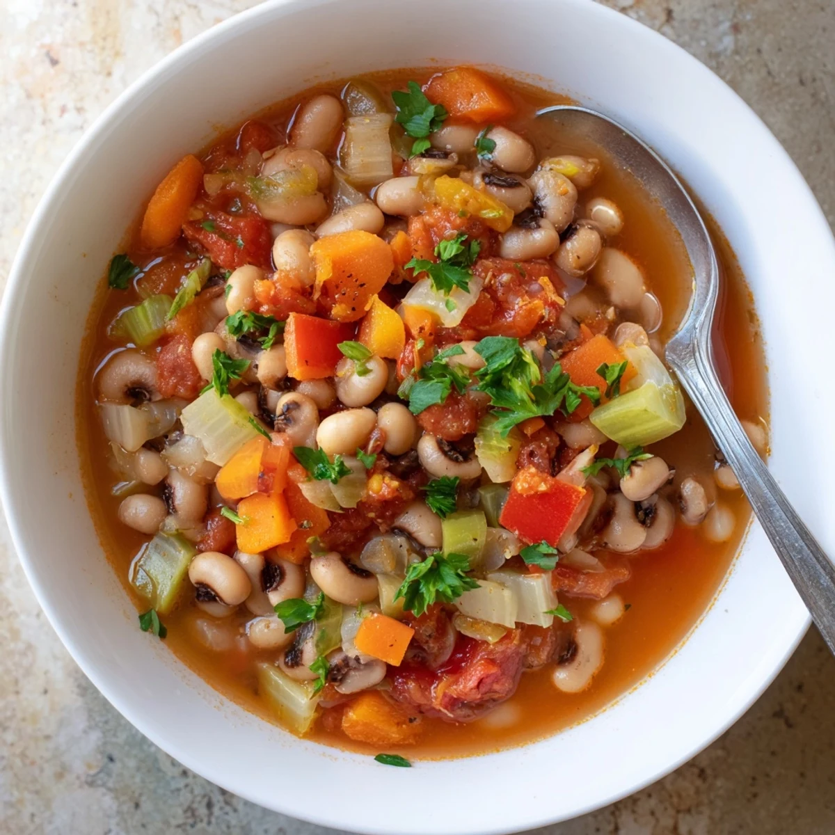 Rich smoky black eyed pea and tomato soup steaming in a white bowl garnished with fresh parsley