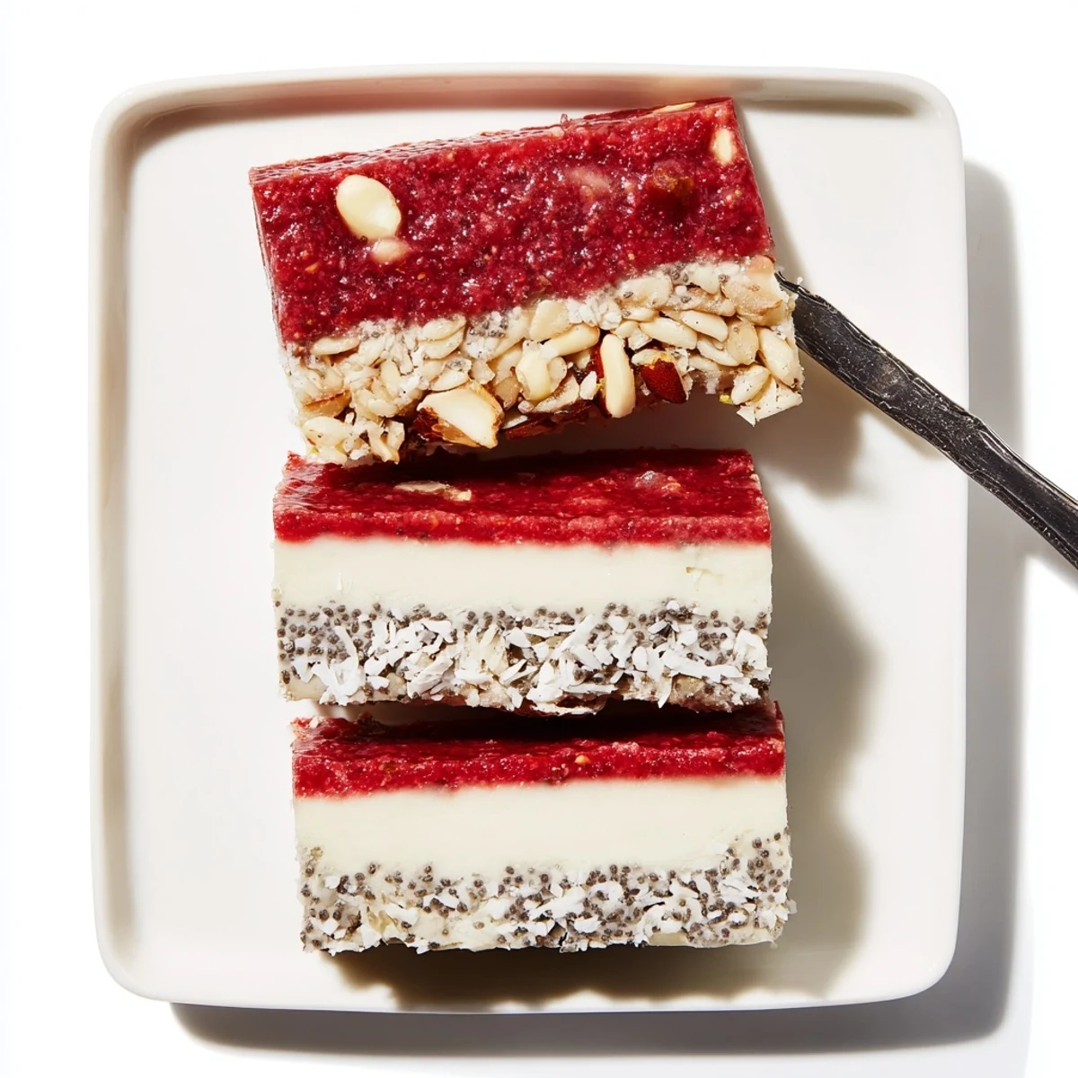 Square pan of strawberry vanilla cashew cream bars with layers of crust and bright red topping