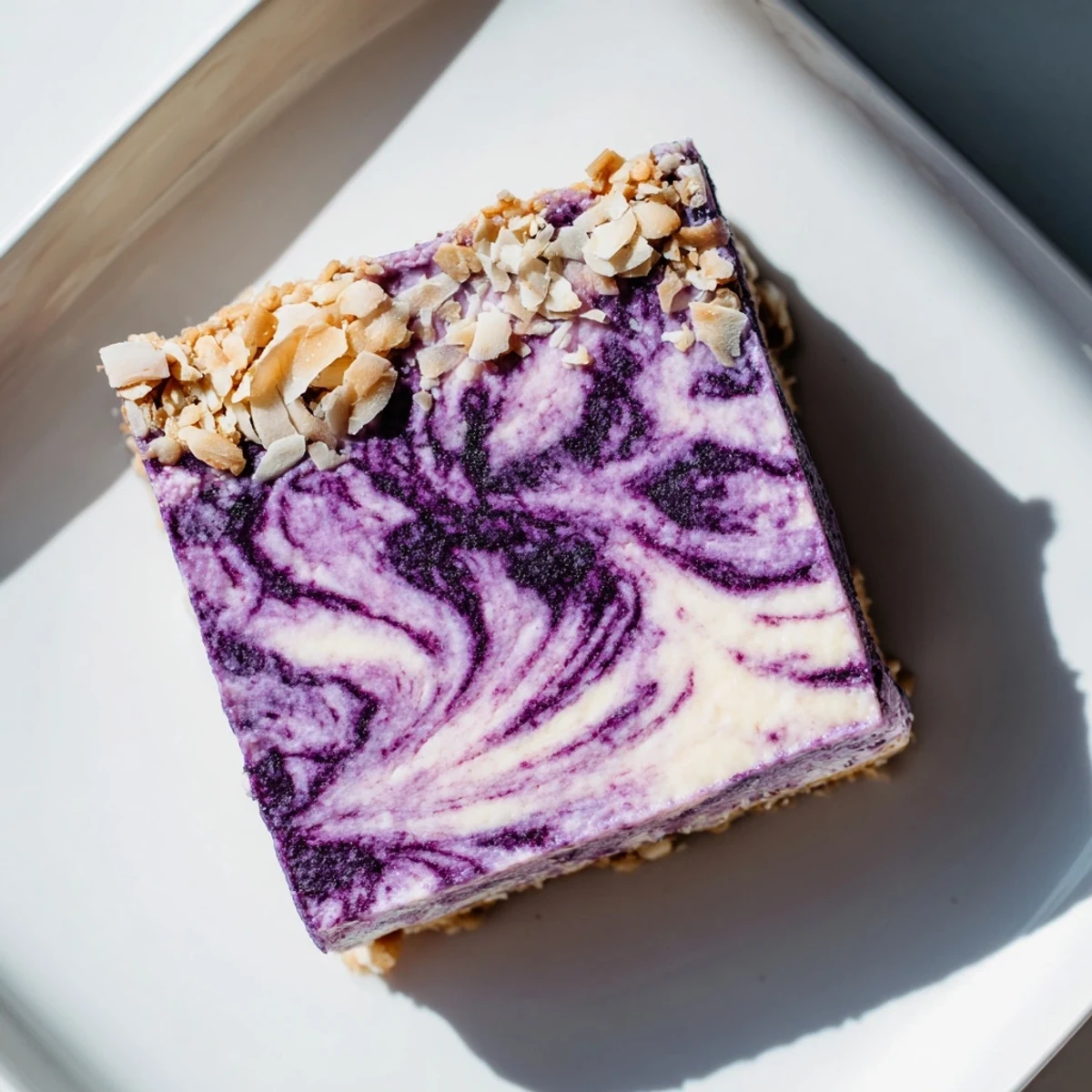 Creamy vegan cashew coconut bars topped with fresh blueberry swirl on a crunchy nut crust
