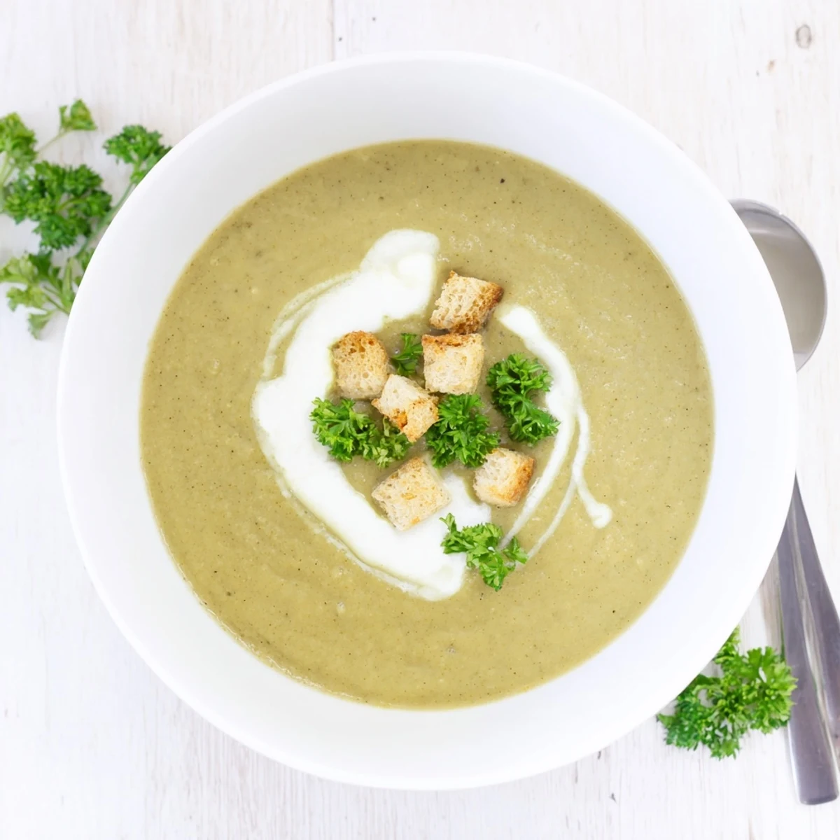 Steaming bowl of hearty white bean and roasted broccoli stem soup with aromatic herbs and crusty bread on side