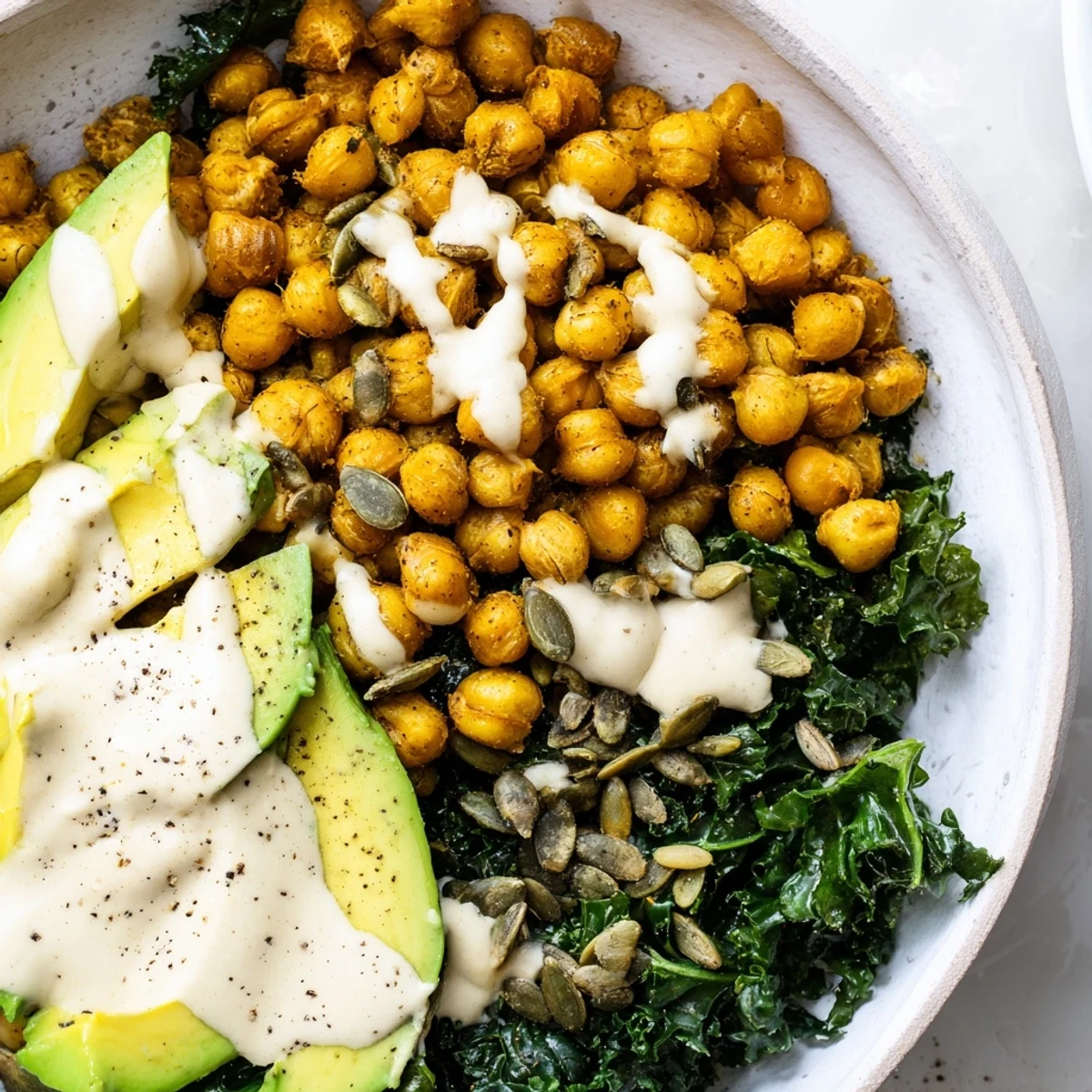 Golden turmeric chickpeas and wilted kale bowl topped with creamy tahini drizzle and sliced avocado