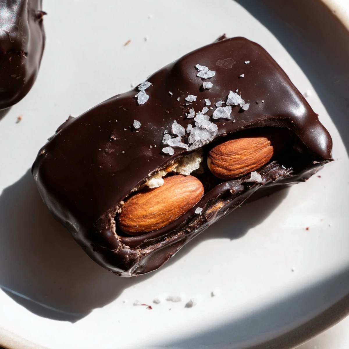 Bite-sized dark chocolate almond butter date clusters arranged on a parchment-lined baking sheet, topped with flaky sea salt