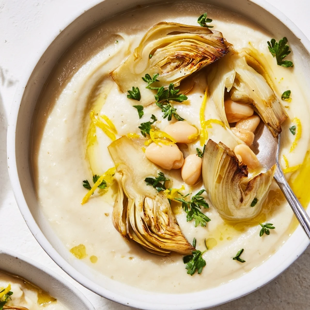 Creamy Roasted Artichoke Heart and White Bean Hearty Soup ladled into bowls, olive drizzled