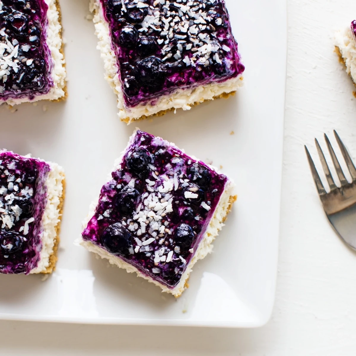 Square slice of blueberry vanilla cashew cream squares featuring purple berry layer over creamy white filling
