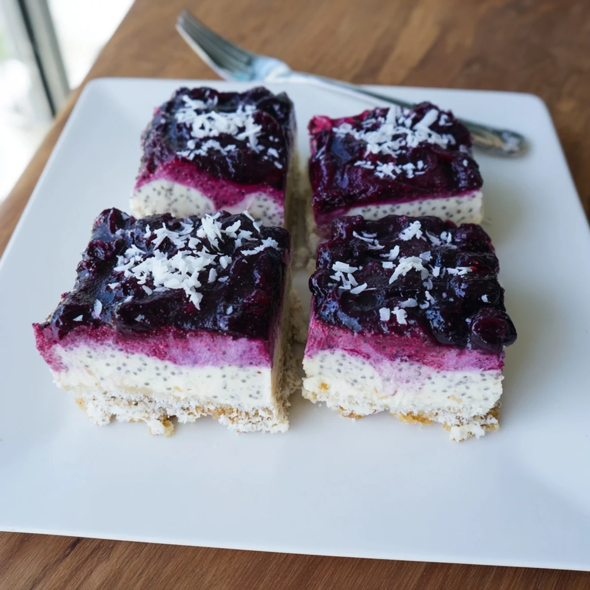 No-bake blueberry vanilla cashew cream squares cut into pieces on white plate with fork