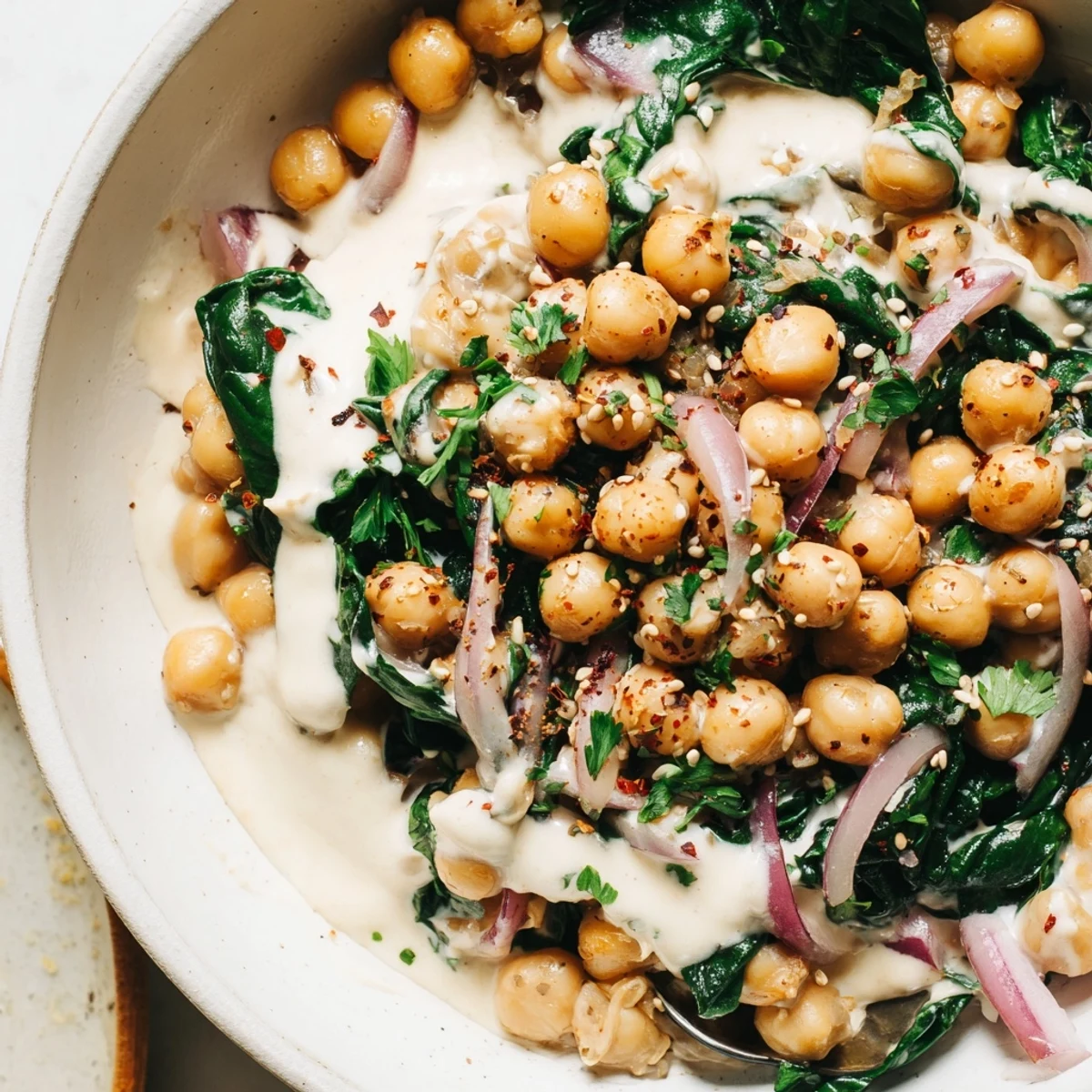 Creamy garlic tahini chickpea and spinach breakfast bowl drizzled with golden sesame sauce